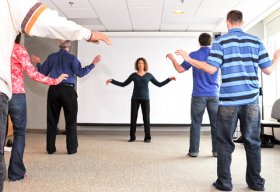 A group of Veterans practice Tai Chi exercises with a woman leader.